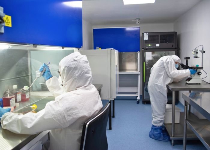 Técnicos de laboratorio con bata blanca realizan controles de calidad en equipos avanzados de terapia celular